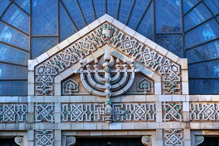 synagogue with intricately patterned stone work on its front, including a menorah above the doors.